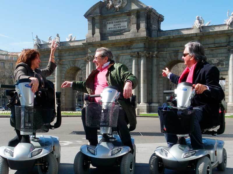 three people in mobility scooter with the door of Alcalá de Madrid background